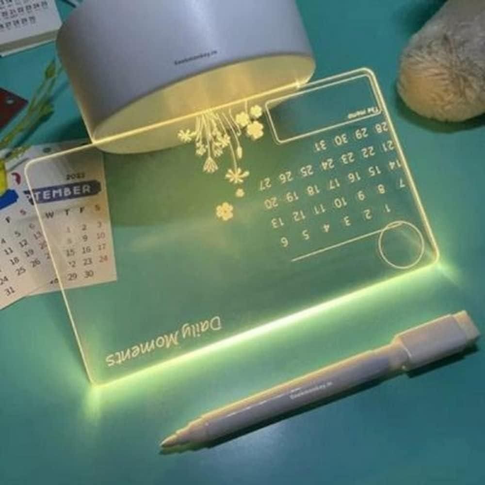 Desk setup with a light-up calendar, pen, and decorative item on a green surface.