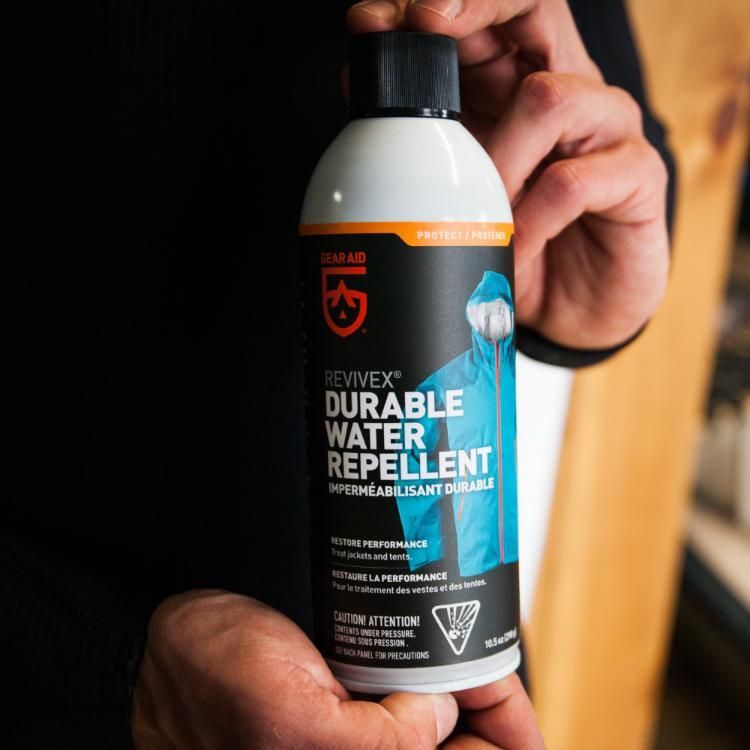 Person holding a bottle of Revivex Durable Water Repellent against a dark background