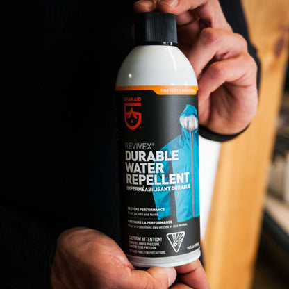 Person holding a bottle of Revivex Durable Water Repellent against a dark background